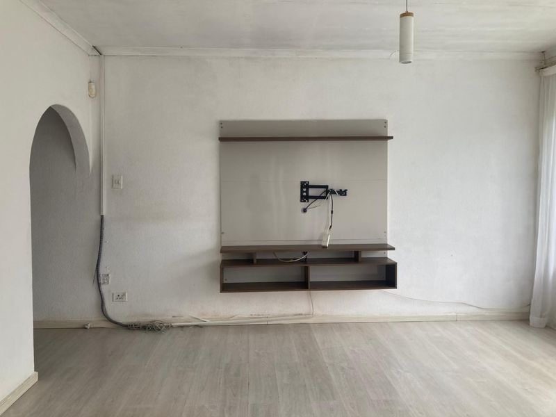 An empty living room featuring a built-in media console, arched doorway, and light-toned laminate flooring, ready for personalization.