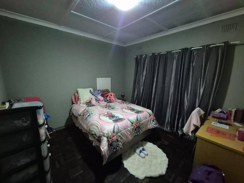 A bedroom featuring dark parquet flooring, ceiling tiles, and neutral wall paint, providing a functional space with standard finishes.