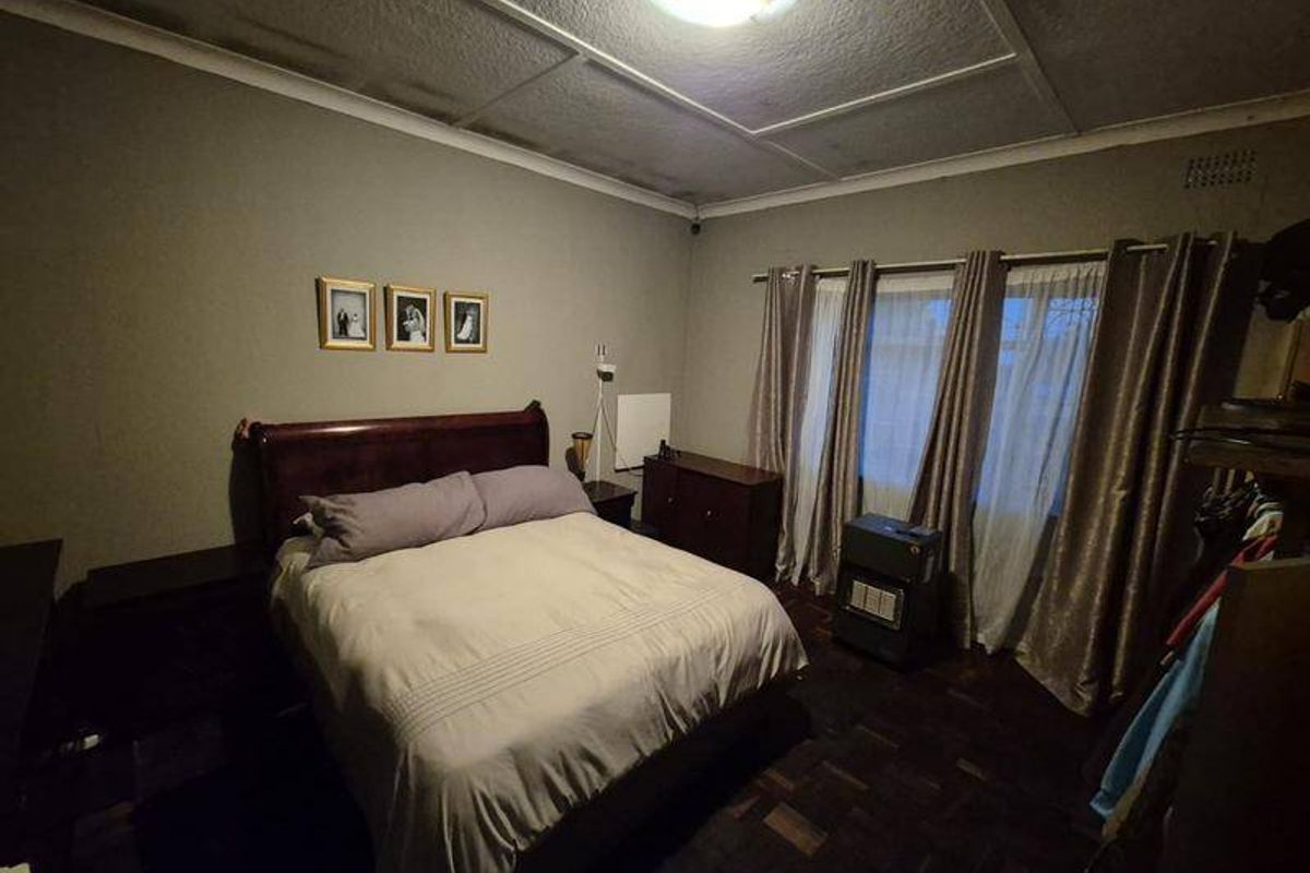 A bedroom featuring dark parquet flooring and a tiled ceiling, offering a functional space with potential for cosmetic updates.