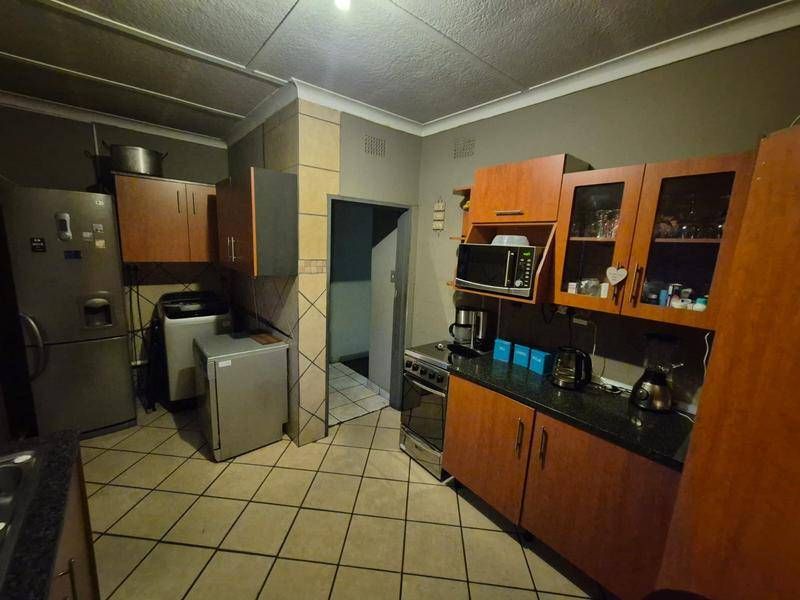 A functional kitchen featuring wood-look cabinetry, dark laminate countertops, tiled flooring, and a dedicated space for appliances.