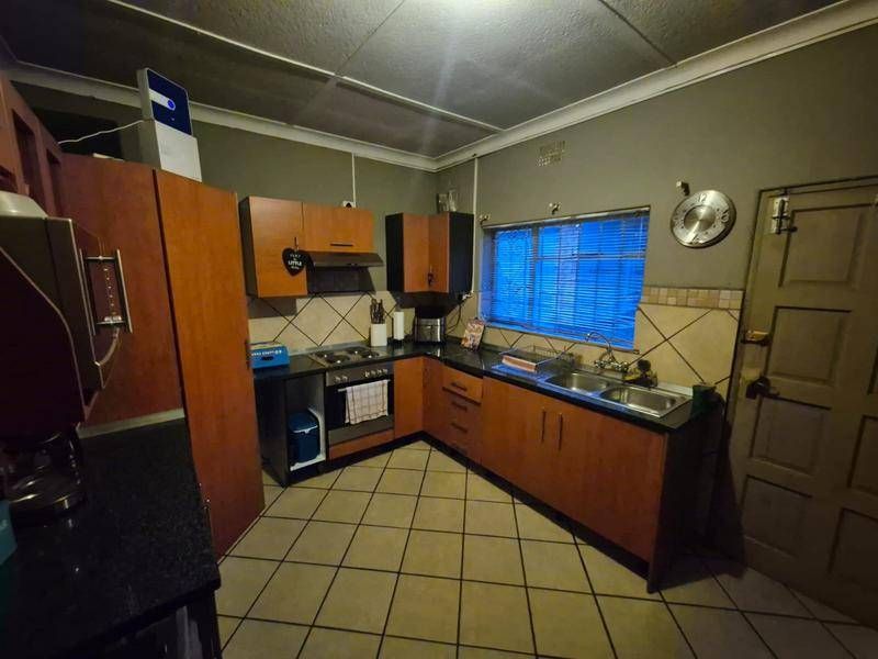 A functional kitchen featuring wood-tone cabinetry, dark countertops, a built-in oven with hob, and tiled flooring, offering a practical layout for daily use.