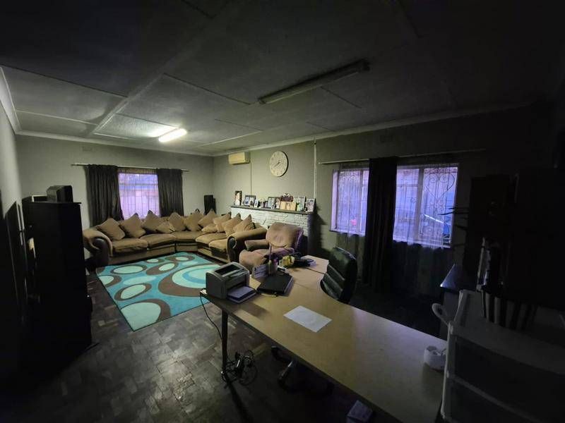 Spacious living area featuring parquet flooring, air conditioning, and security bars on windows. The room offers a versatile layout for lounge and office use.