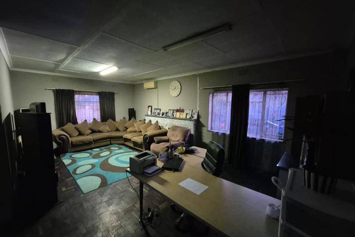 Spacious living area featuring parquet flooring, air conditioning, and security bars on windows. The room offers a versatile layout for lounge and office use.