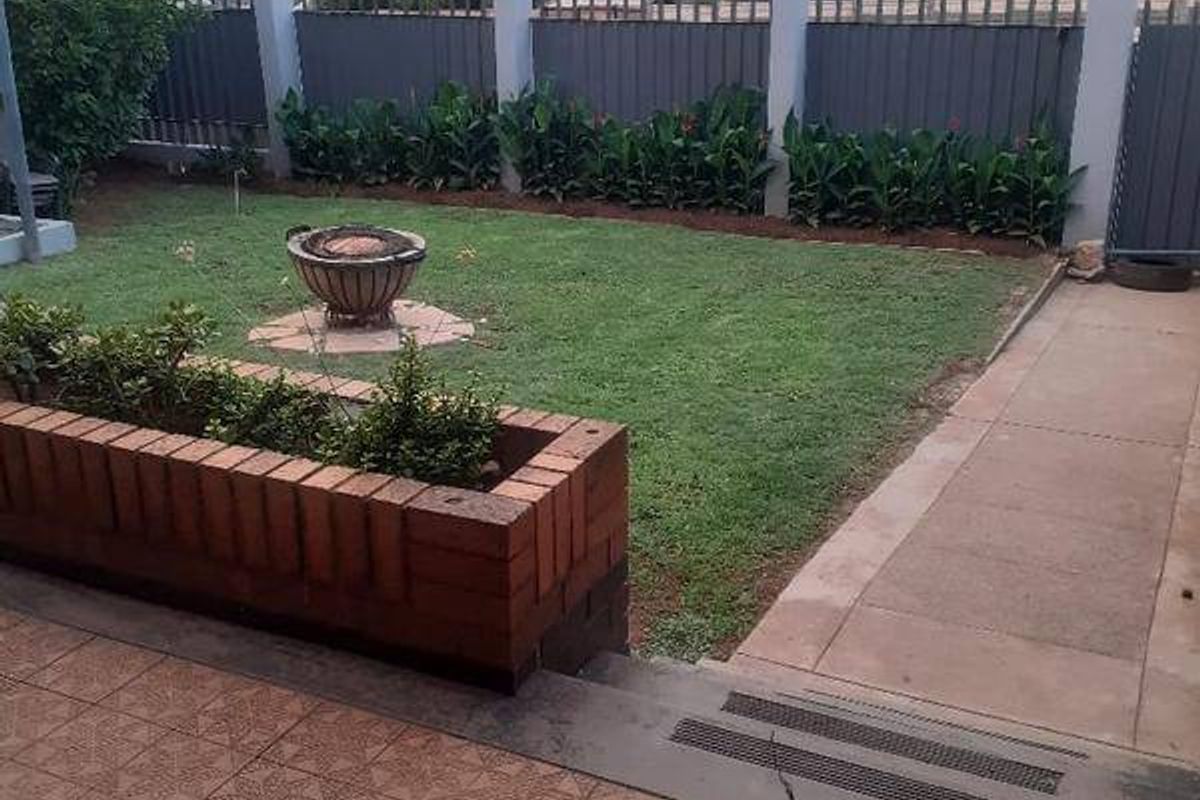 A private rear garden featuring a tiled patio, a brick planter box, a well-maintained lawn, and secure metal perimeter fencing.