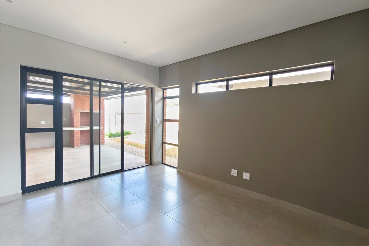 A bright, modern living area featuring large aluminium sliding doors that open onto a covered patio with a built-in brick braai.