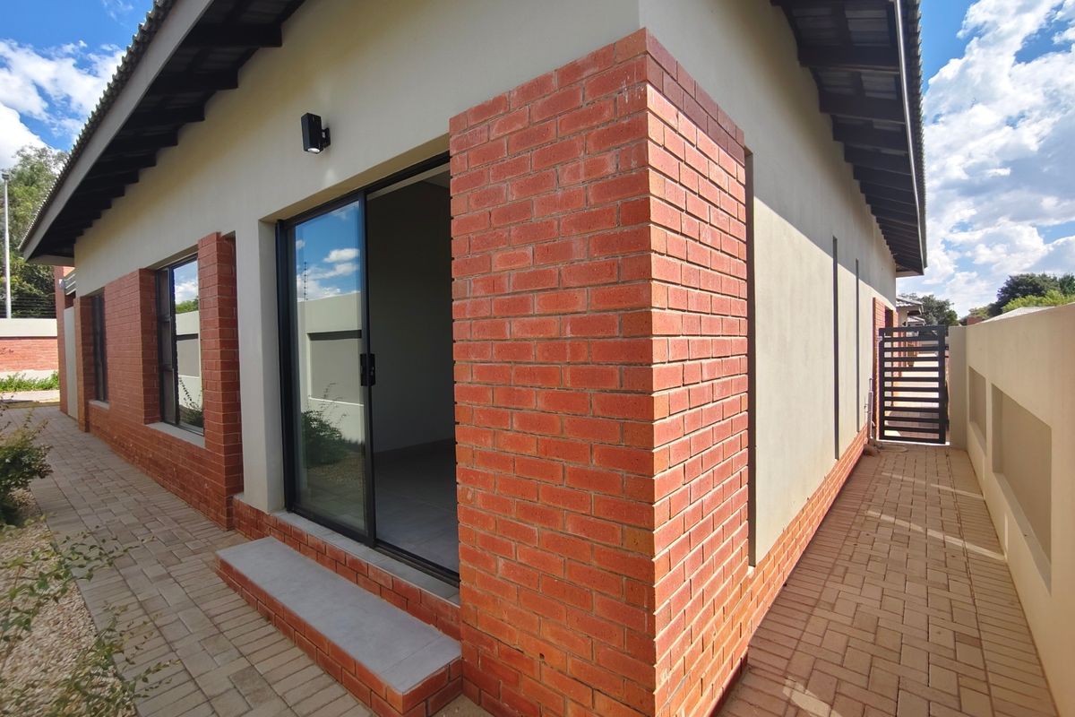 Rear exterior view of the townhouse featuring exposed brick detailing, paved walkways, and a sliding glass door providing access to the interior.