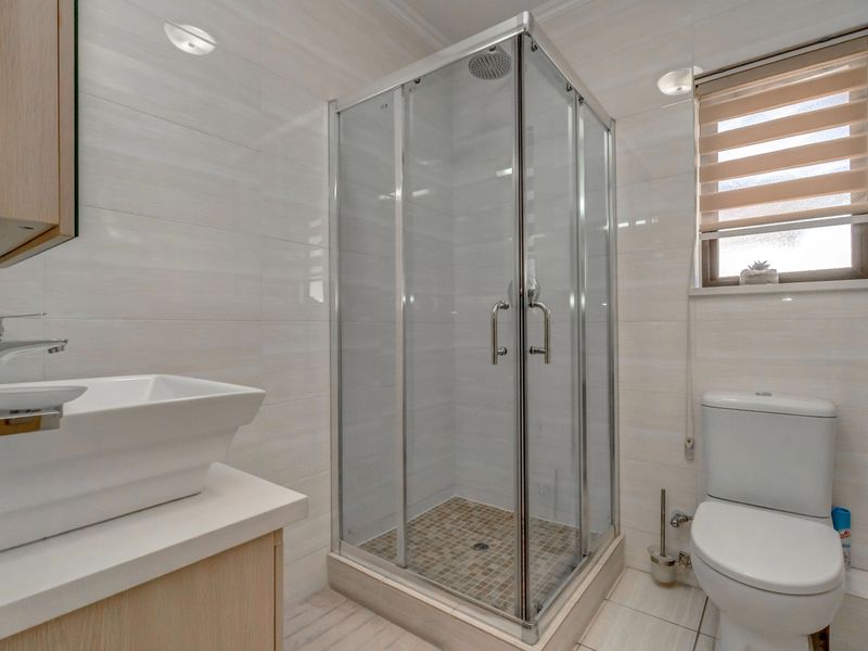 Modern bathroom featuring a glass-enclosed corner shower, a contemporary vessel sink vanity, and a standard toilet with neutral wall tiling.