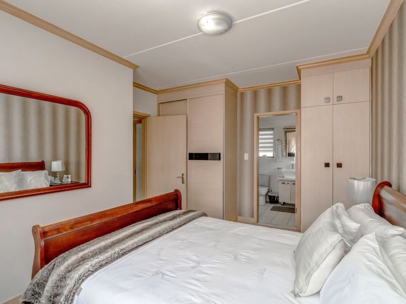A well-maintained bedroom featuring built-in cabinetry, crown molding, and an en-suite bathroom with tiled flooring.