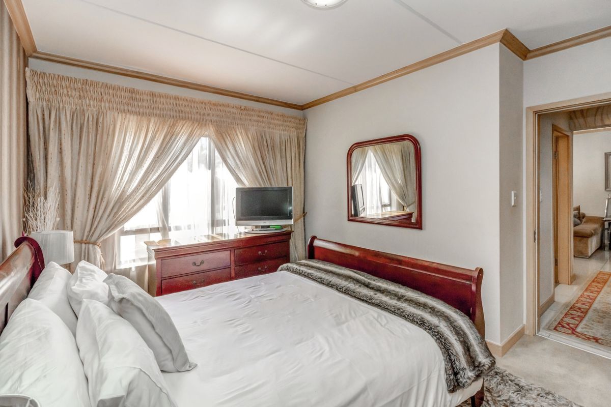 A well-maintained bedroom featuring neutral walls, crown molding, and a large window with natural light, providing a comfortable and functional living space.