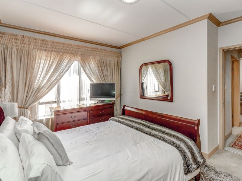 A well-maintained bedroom featuring neutral walls, crown molding, and a large window with natural light, providing a comfortable and functional living space.