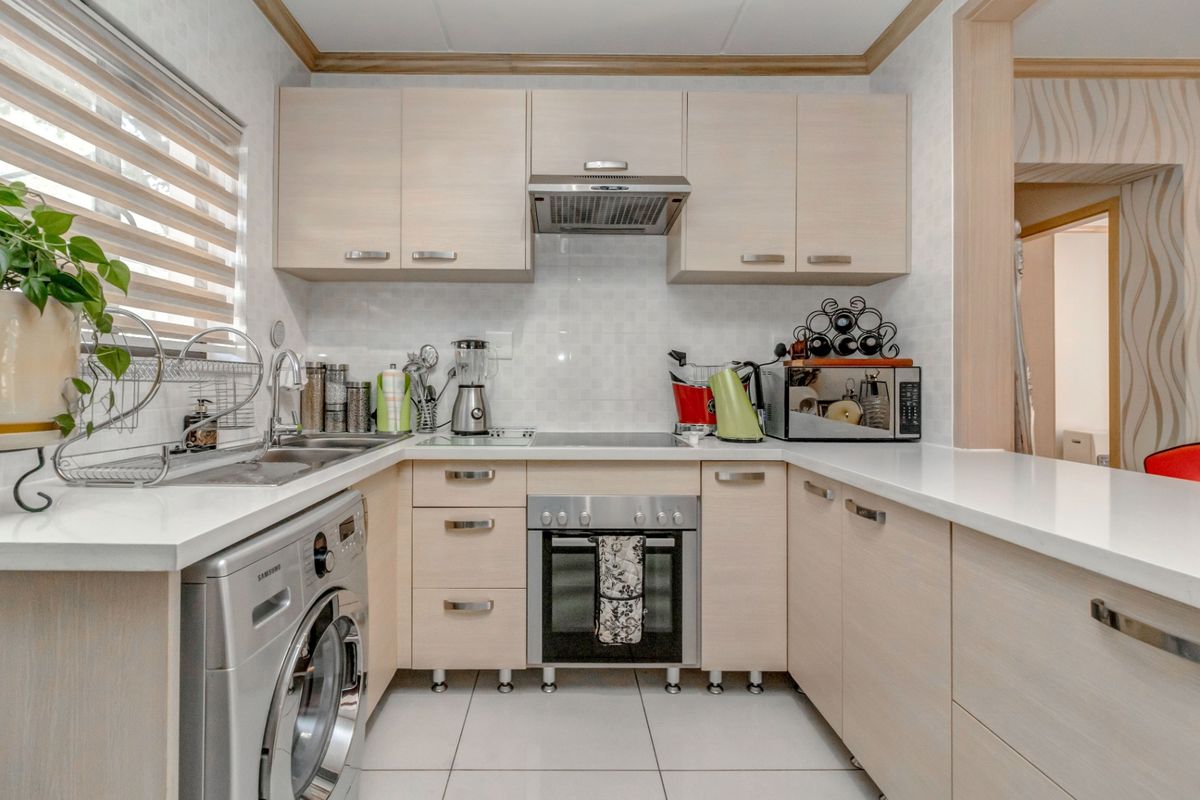 Compact kitchen featuring light wood cabinetry, white countertops, tiled backsplash, built-in oven, extractor fan, and integrated laundry appliance space.