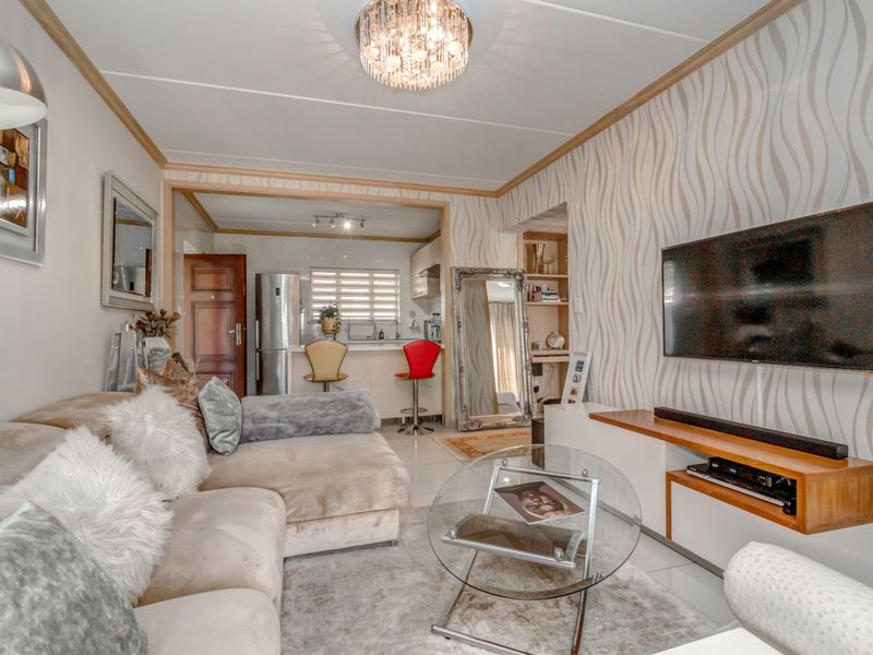 Open-plan living area featuring a modern kitchen with breakfast bar, tiled flooring, and decorative wallpaper, seamlessly connecting to the lounge space.