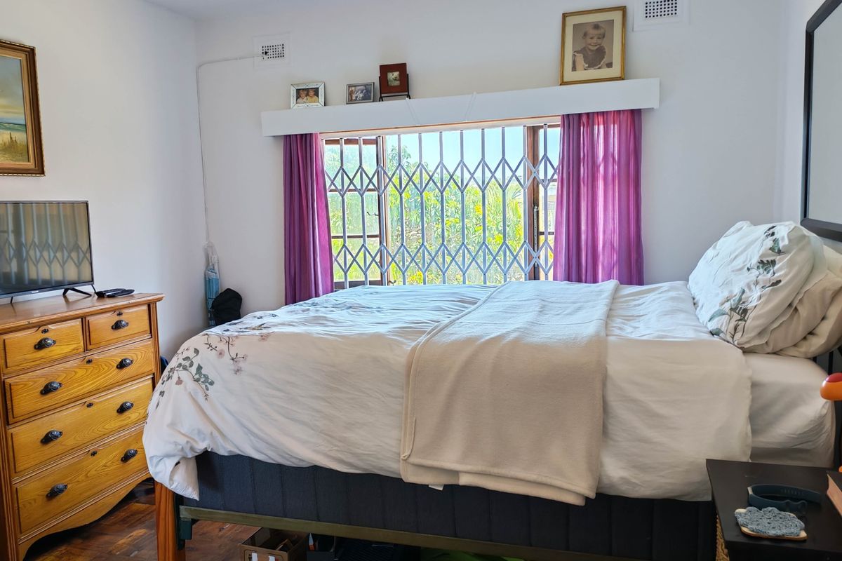 A bedroom featuring timber flooring and a window fitted with a security gate, providing natural light and ventilation.