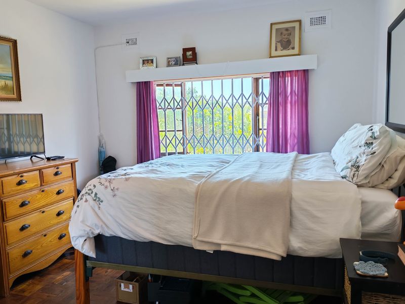 A bedroom featuring timber flooring and a window fitted with a security gate, providing natural light and ventilation.