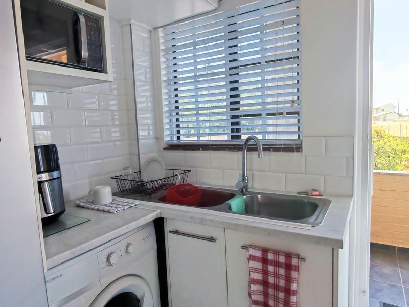 Compact kitchen area featuring white subway tile backsplash, stainless steel sink with mixer tap, laminate countertops, and built-in microwave cabinetry.