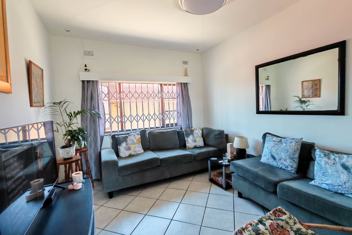 A comfortable living room featuring ceramic floor tiles, a large window with a security gate, and neutral wall finishes.