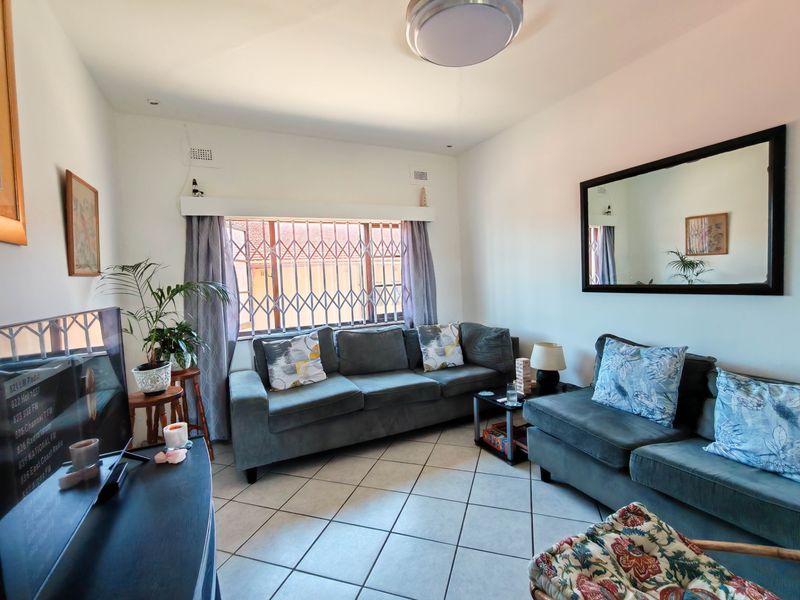 A comfortable living room featuring ceramic floor tiles, a large window with a security gate, and neutral wall finishes.