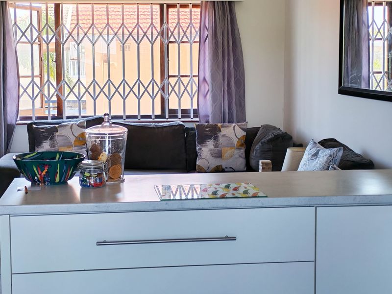Open plan living area featuring modern white cabinetry, a sleek countertop, and a window fitted with a security gate.