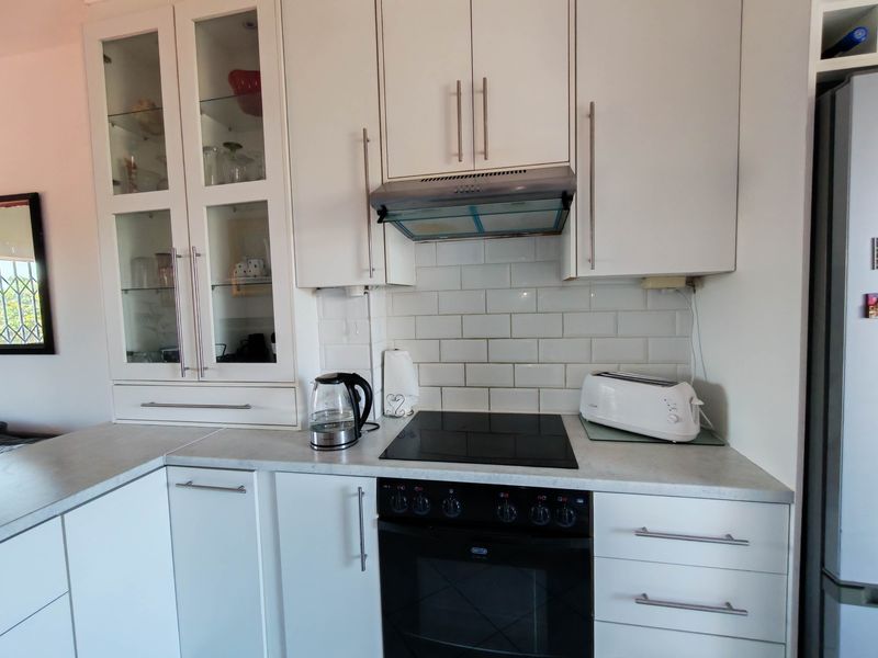 A functional kitchen featuring white cabinetry, subway tile backsplash, integrated electric hob, oven, and extractor fan with ample storage space.