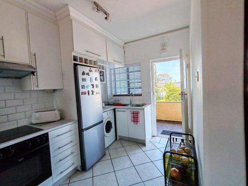 Compact kitchen featuring white cabinetry, subway tile backsplash, built-in oven and hob, and direct access to an outdoor balcony area.
