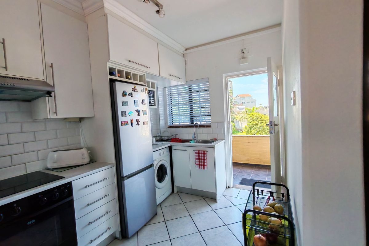 Compact kitchen featuring white cabinetry, subway tile backsplash, built-in oven and hob, and direct access to an outdoor balcony area.