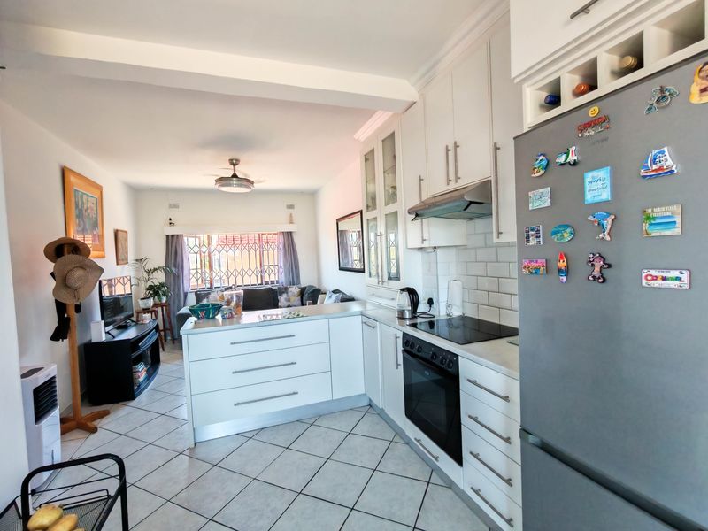 Open-plan living area featuring a modern kitchen with white cabinetry, subway tile backsplash, built-in oven, and hob, flowing into a comfortable lounge space.