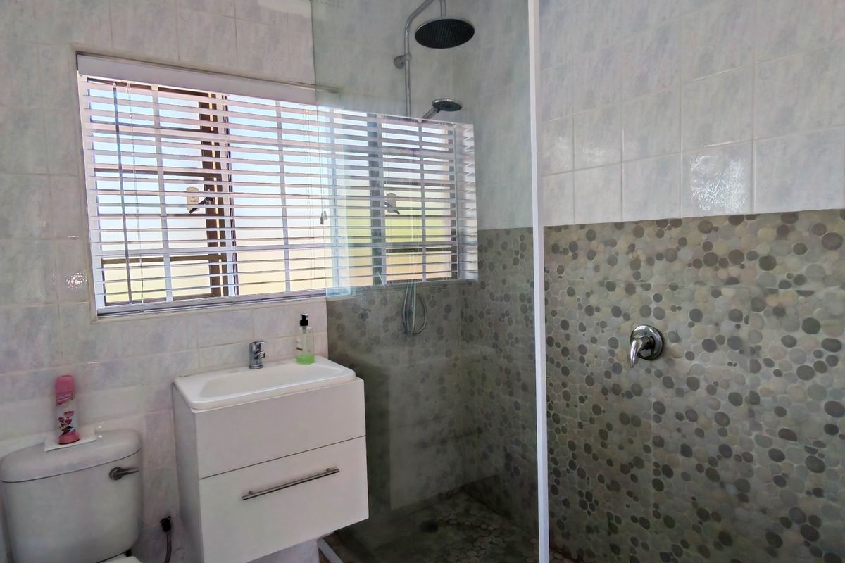 A modern bathroom featuring a glass-enclosed shower with a rainfall shower head, a wall-mounted vanity, and a decorative mosaic tile feature wall.
