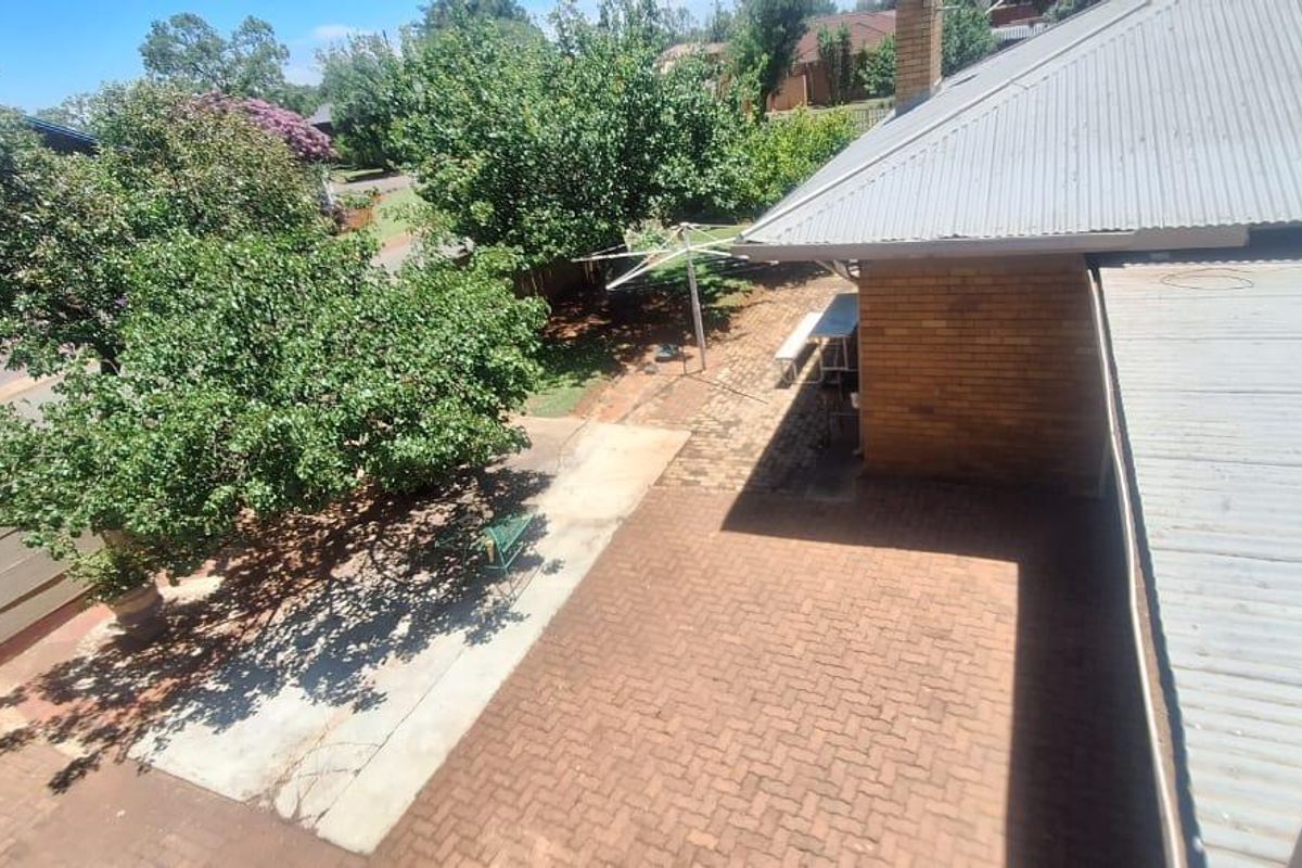 An elevated view of the rear yard featuring a brick-paved patio area, established trees, and a corrugated metal roof structure.
