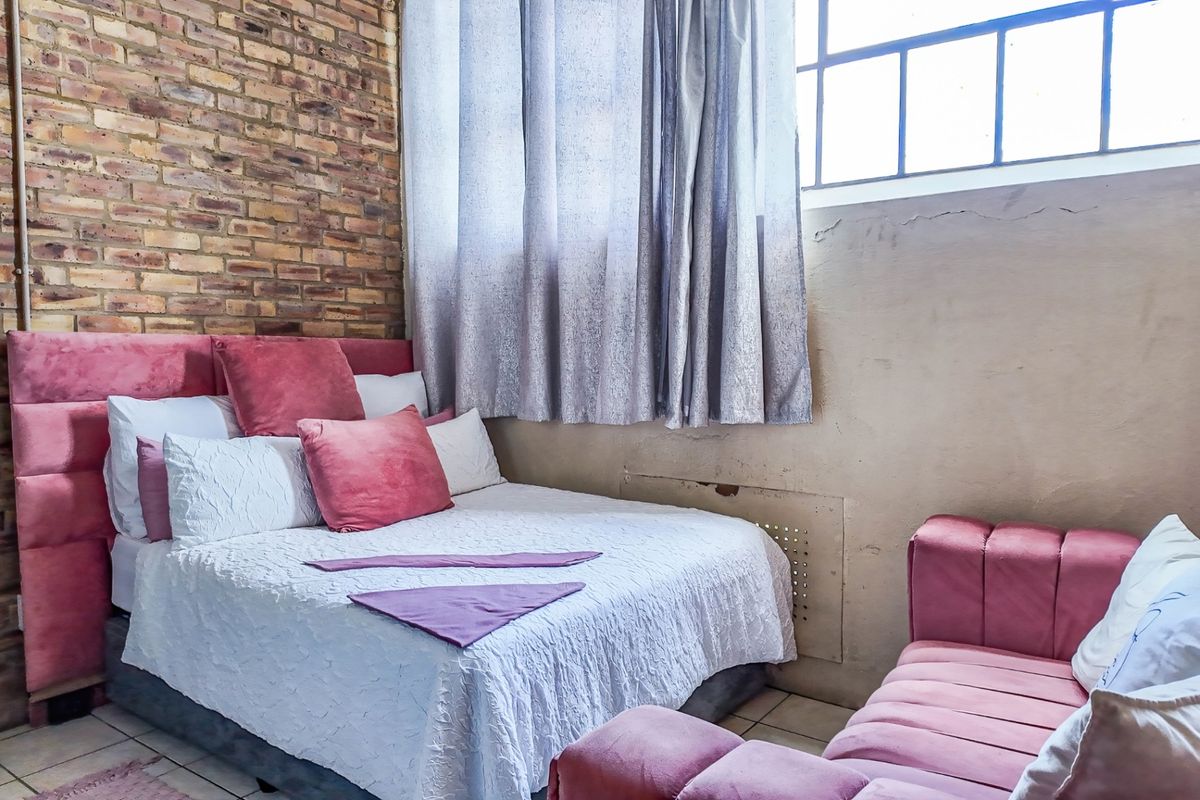 Bedroom featuring an exposed brick feature wall, tiled flooring, and a high-level window providing natural light.