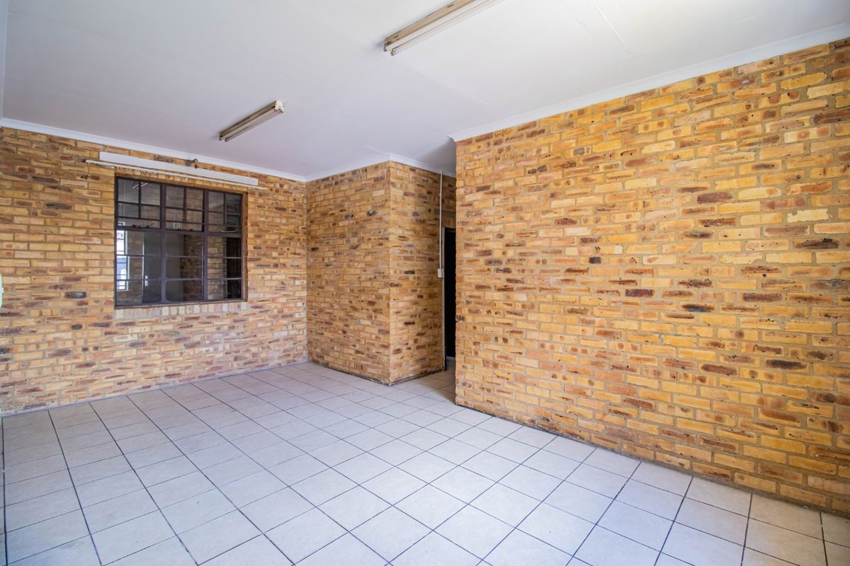 An empty living area featuring exposed brick walls, ceramic tiled flooring, and steel-framed windows, offering a blank canvas for renovation.