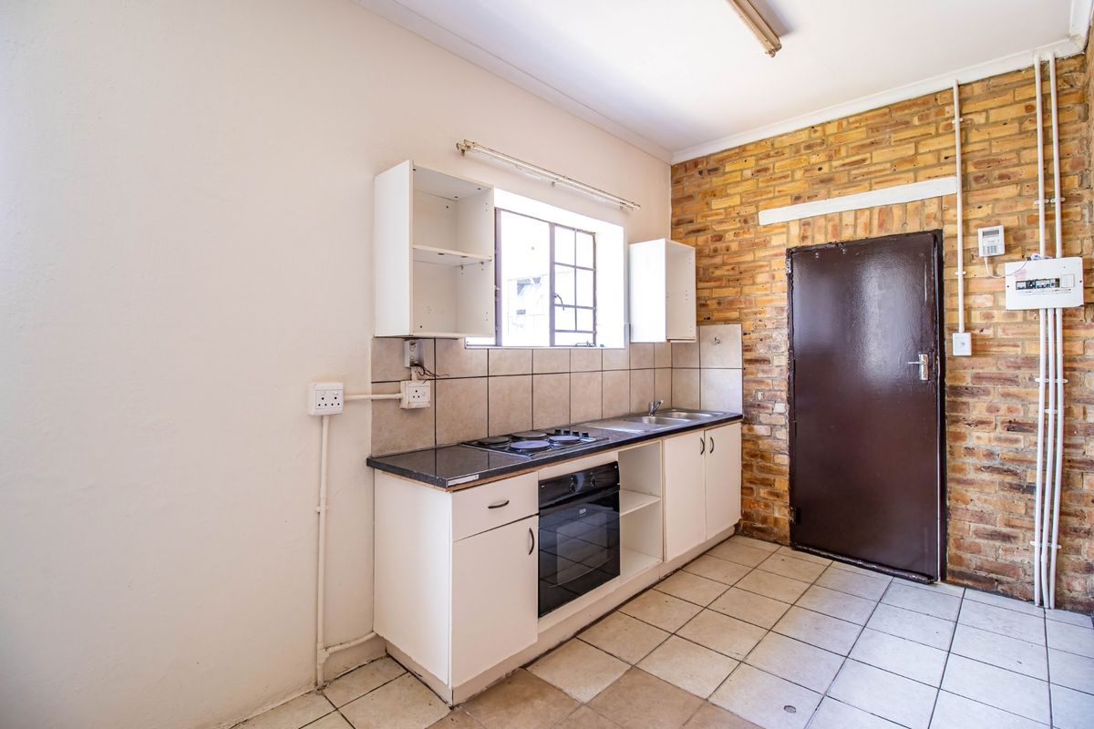 A functional kitchen featuring built-in cabinetry, an integrated oven and hob, tiled backsplash, and an exposed brick feature wall.