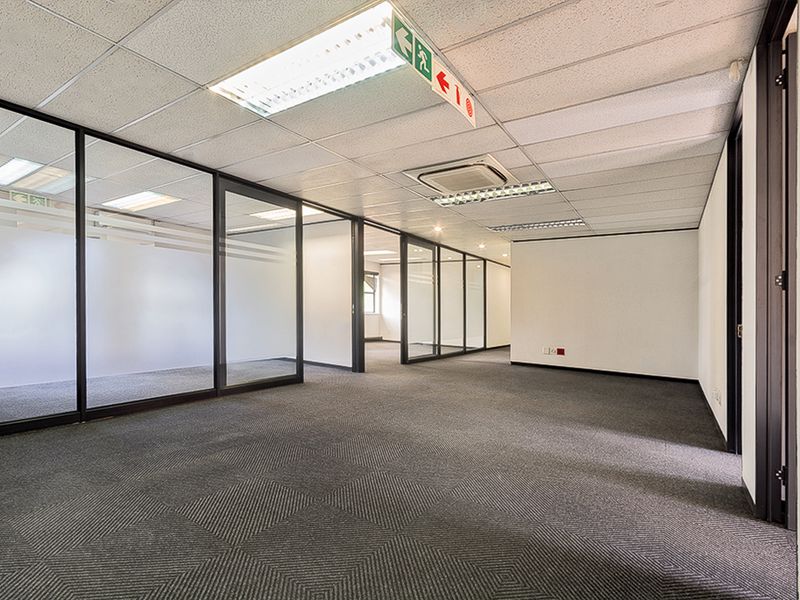 A modern, vacant commercial office space featuring glass partitions, suspended ceilings with recessed lighting, and carpeted flooring, suitable for a professional workspace.