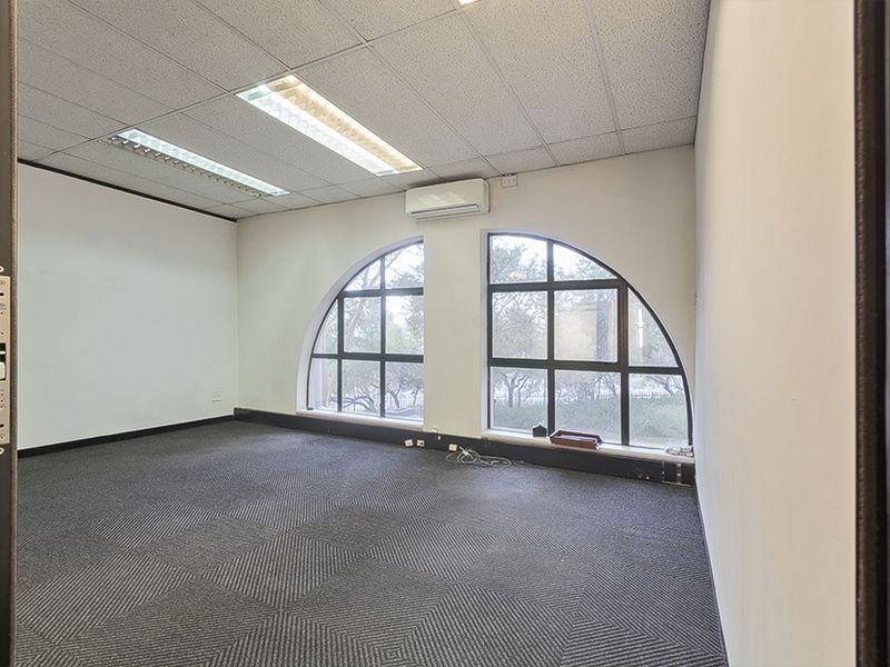 Empty commercial office space featuring arched windows, suspended ceiling with recessed lighting, split-system air conditioning, and dark carpet tiles.