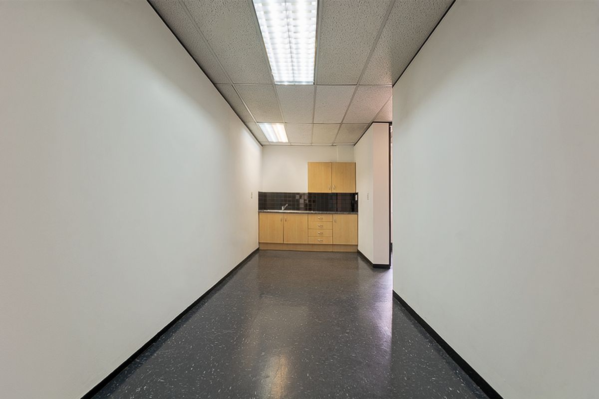 A functional commercial kitchenette featuring built-in cabinetry, a stainless steel sink, and durable vinyl flooring within a clean, open-plan office environment.