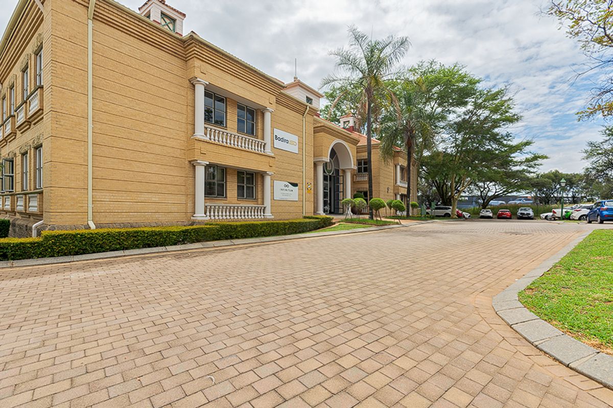 Front exterior view of a multi-story commercial building featuring a brick facade, decorative columns, balustrades, and a paved driveway entrance.