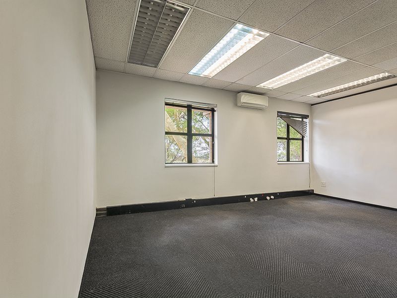 A vacant commercial office space featuring a suspended ceiling, recessed lighting, split-system air conditioning, and dark carpeted flooring.