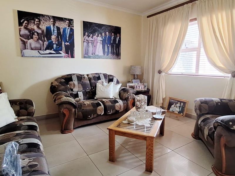 A comfortable living room featuring neutral tiled flooring and natural light through a window with fitted curtain rails.
