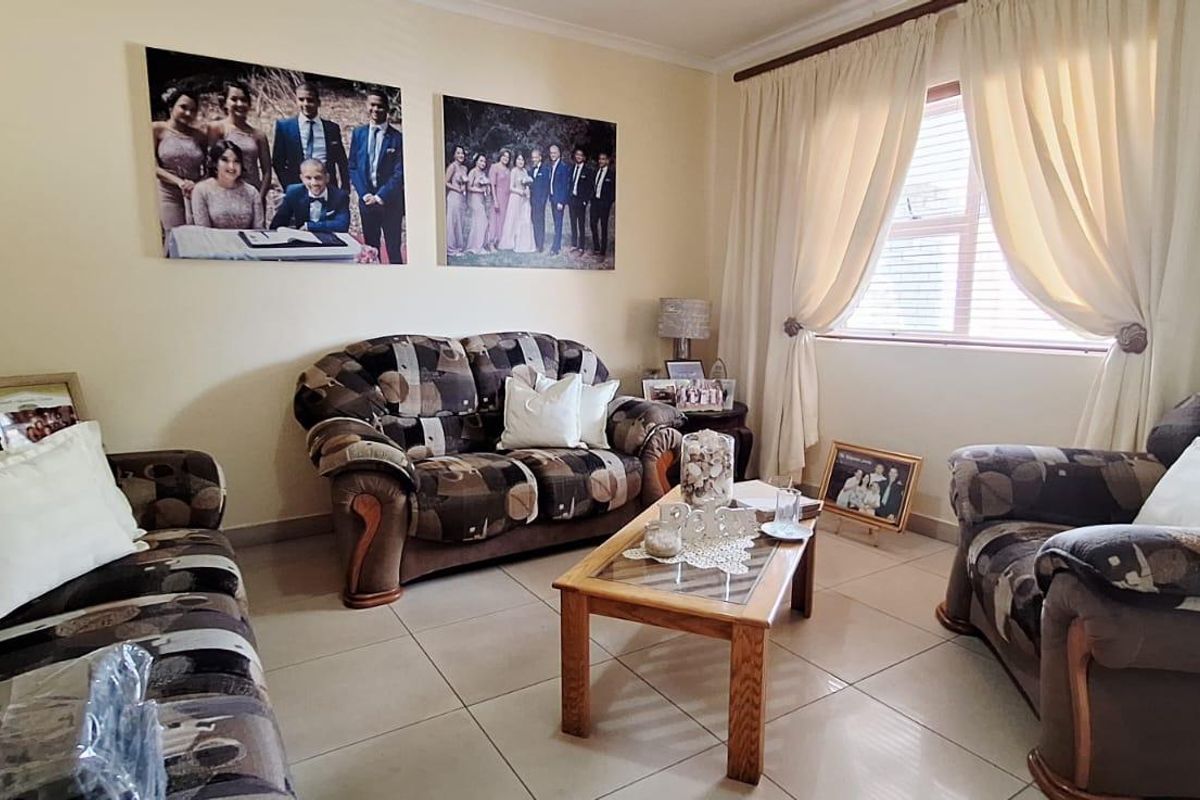 A comfortable living room featuring neutral tiled flooring and natural light through a window with fitted curtain rails.