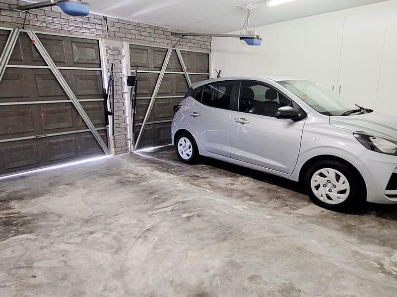 Spacious double garage featuring exposed brickwork, automatic door mechanisms, and extensive built-in storage cabinetry.