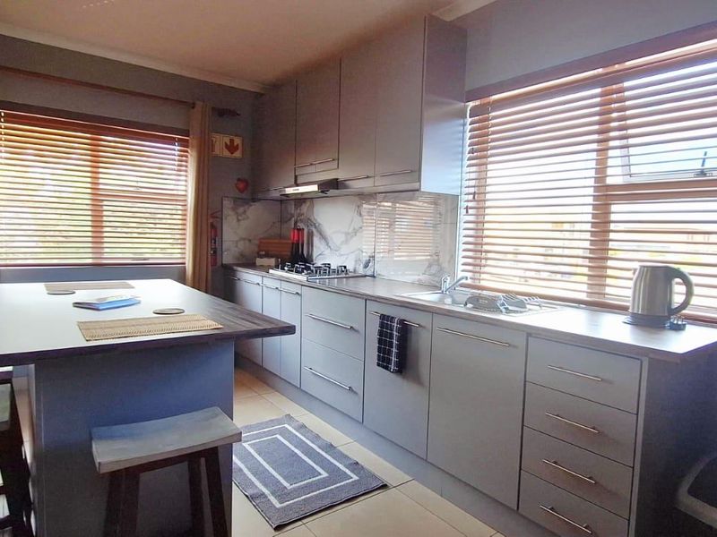 Modern kitchen featuring grey cabinetry, stone countertops, a marble-look splashback, and an integrated hob with extractor fan, complemented by natural light from venetian blinds.