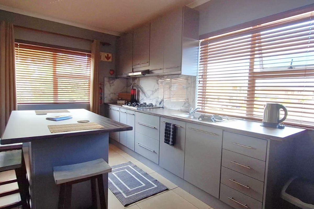 Modern kitchen featuring grey cabinetry, stone countertops, a marble-look splashback, and an integrated hob with extractor fan, complemented by natural light from venetian blinds.
