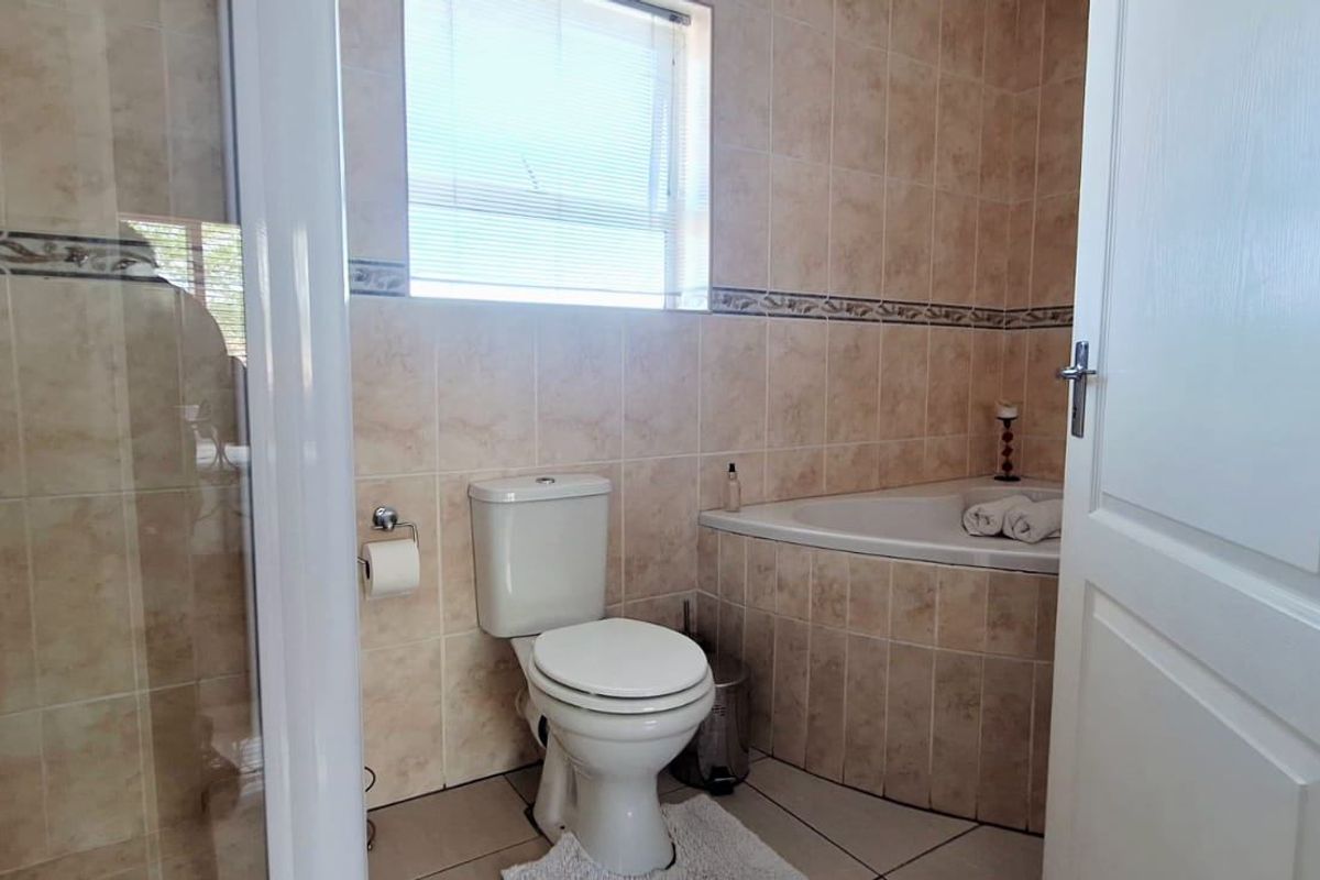 A functional bathroom featuring a built-in bathtub, separate shower enclosure, and neutral ceramic tiling throughout.