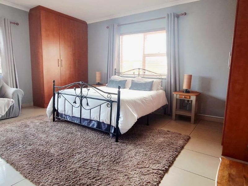 Spacious bedroom featuring neutral tiled flooring, built-in wooden cupboards, and an integrated air conditioning unit for climate control.