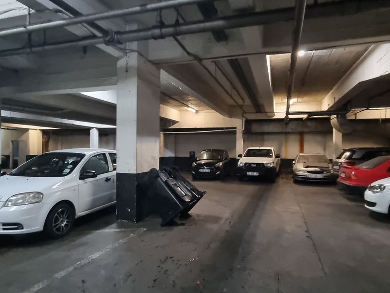 Underground parking garage area featuring concrete structural columns, exposed overhead utility piping, and a wall-mounted fire hose reel.