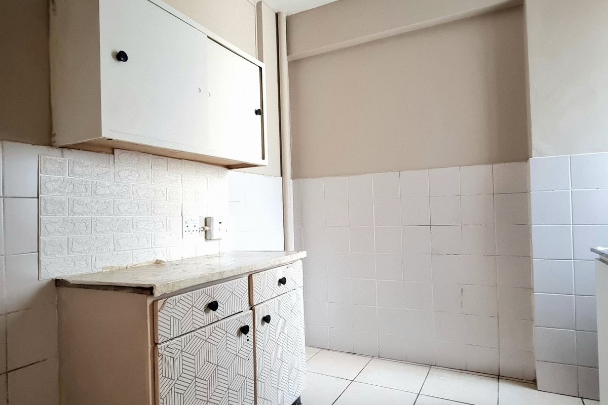 A compact, empty kitchen featuring built-in cabinetry, tiled backsplash, and tiled flooring, offering a blank canvas for renovation and modernization.