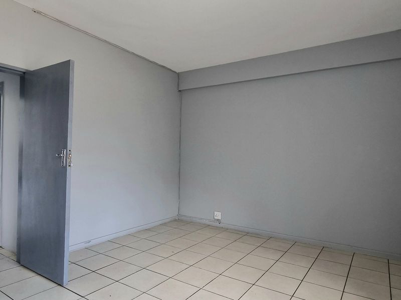 An empty bedroom featuring neutral grey walls, tiled flooring, and built-in cupboards, offering a blank canvas for personalization.