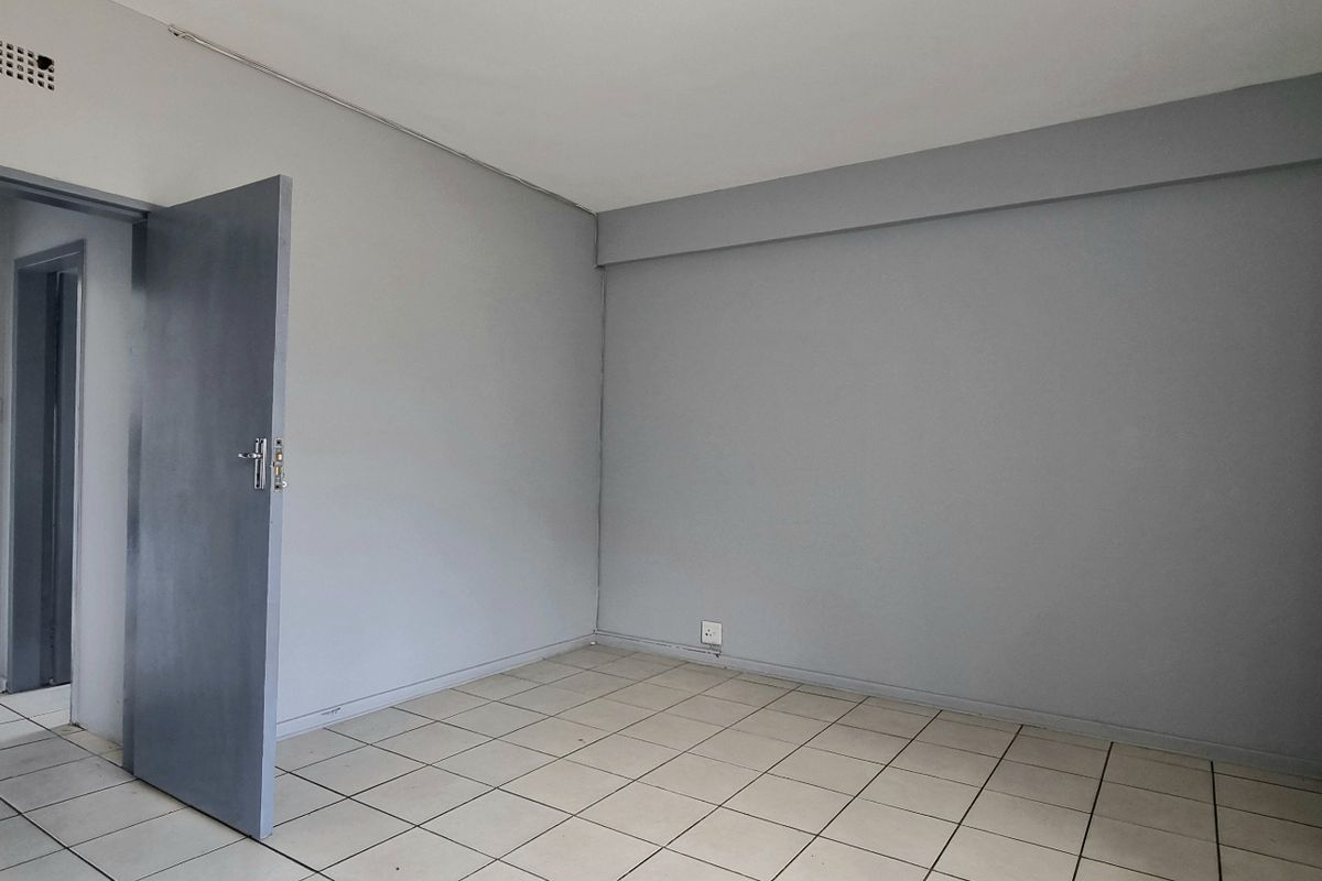 An empty bedroom featuring neutral grey walls, tiled flooring, and built-in cupboards, offering a blank canvas for personalization.