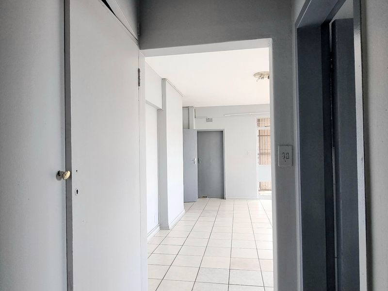 A vacant hallway featuring tiled flooring and a built-in cupboard, providing access to adjacent rooms within the apartment.