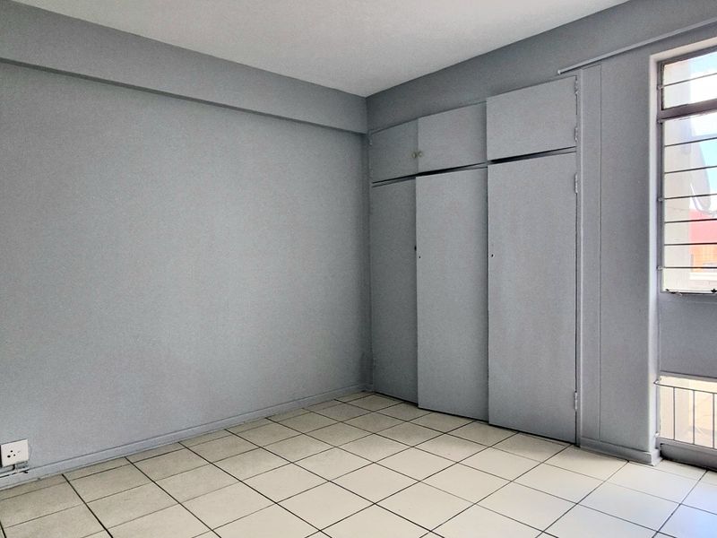 An empty bedroom featuring tiled flooring, built-in cupboards, and a large window with security bars, offering a neutral canvas for potential updates.