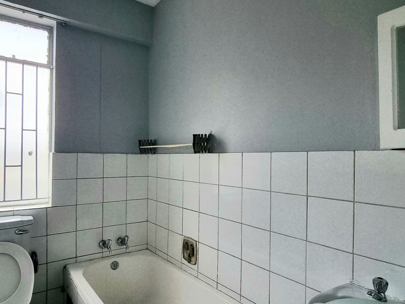 A dated bathroom featuring a standard bathtub, toilet, and basin with tiled walls and security bars on the window.